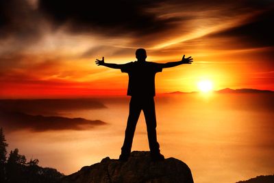 Silhouette man with arms raised against sky during sunset