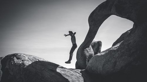 Low angle view of man jumping over boulder against sky