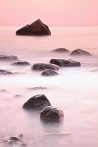 Rocks in sea against sky during sunset