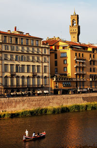 Tourists riding boat on arno river by palazzo vecchio in tuscany