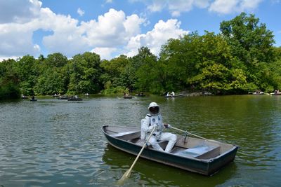 Spacesuit sitting in boat on river against sky