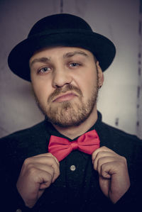 Portrait of man holding bow tie while standing against wall