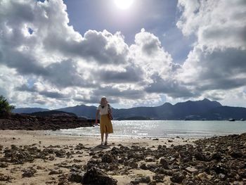 Rear view of woman standing on beach against sky