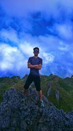 Full length portrait of man standing on mountain against cloudy sky