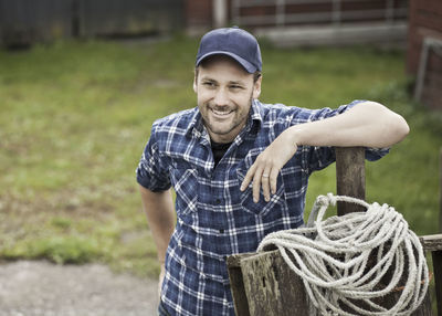 Smiling farmer looking away while leaning on railing at farm