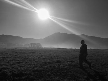 Side view of man walking on field against sky during sunny day