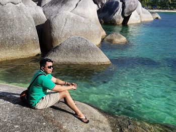 Full length of man sitting on rock by sea at belitung island during sunny day