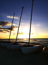 Sailboats moored on sea against sky during sunset