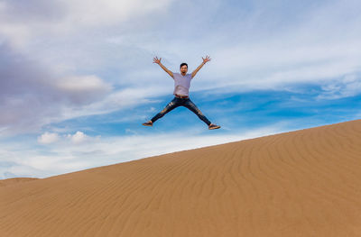 Man jumping over desert against sky