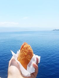 Midsection of person holding ice cream against sea