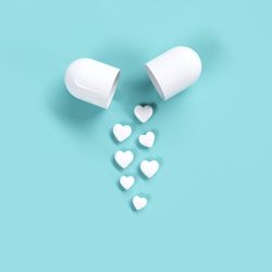 High angle view of heart shape pills by open capsule against blue background