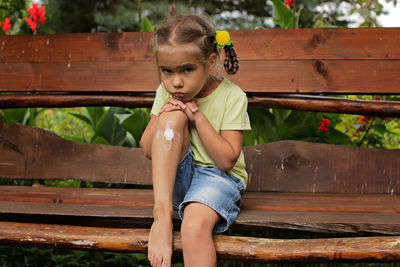 Portrait of cute girl with injured knee sitting on bench