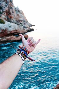 Close-up of woman hand on rock in sea against clear sky