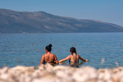 Rear view of shirtless men in sea against sky