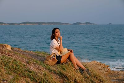 Woman sitting on shore against sky