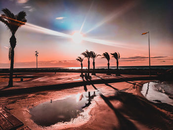 Silhouette palms by sea against sky during sunset