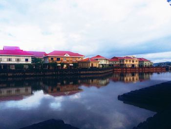 Reflection of houses in calm lake against cloudy sky