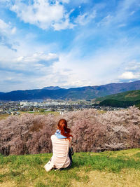 Rear view of woman sitting on mountain against sky