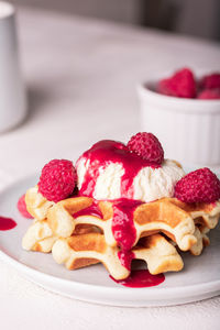 Freshly baked waffles with raspberry syrup and ice cream on a plate