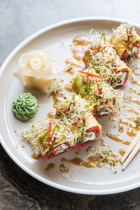 Fresh tasty sushi with greens on white plate on table