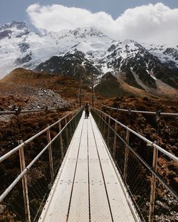 Young man standing on footbridge against snowcapped mountain