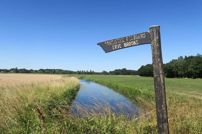 Information sign on field against clear blue sky