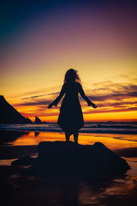Silhouette woman standing at beach against sky during sunset