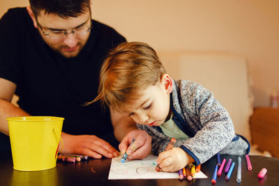 Father and son coloring on table at home