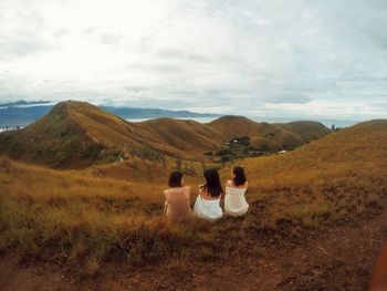 Rear view of female friends sitting on mountain against sky