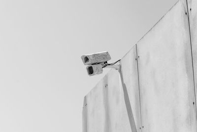 Low angle view of security camera on wall against sky