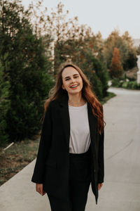 Young woman in black trouser suit and silver shoes on the background of the park