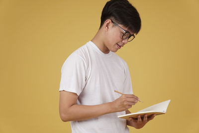 Midsection of man holding eyeglasses against yellow wall