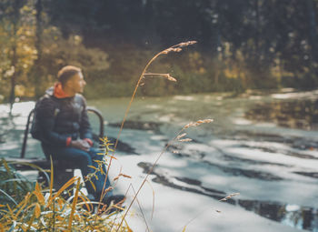 Defocused image of man sitting by water during winter in forest