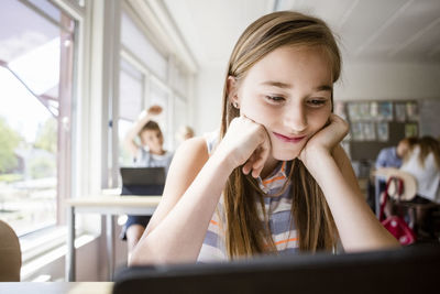 Schoolgirl reading from digital tablet at desk in classroom