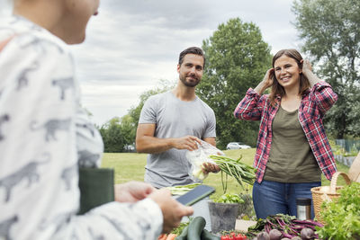 Mid adult couple looking at female customer at vegetable garden