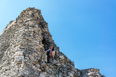 Low angle view of person on rock against clear blue sky