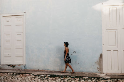 Woman in hat walking against house
