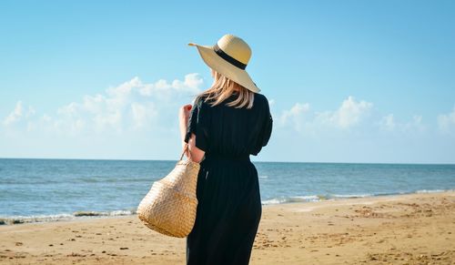 Man wearing hat standing on beach against sky