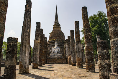 Ruined pagoda and buddha statue on field against clear blue sky