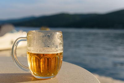 Mug of cold beer on table in bar by sea