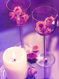 High angle view of wineglasses with roses by candle on table