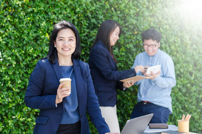 Portrait of smiling businesswoman with coffee against colleagues discussing at cafe