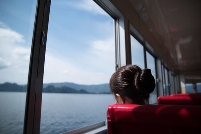 Rear view of woman looking through window while traveling in vehicle