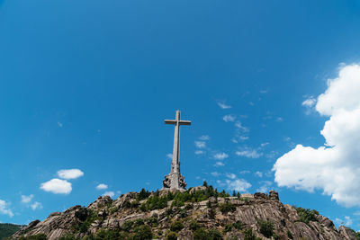 Low angle view of cross on rock against blue sky during sunny day