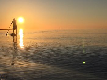 Silhouette man standing in sea against sky during sunset