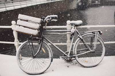 Snow covered bicycle parked on bridge over canal