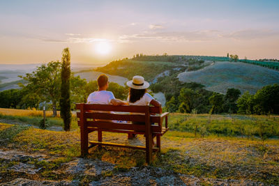 Rear view of people sitting on bench looking at sunset