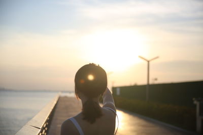 Rear view of woman on street against sky during sunset