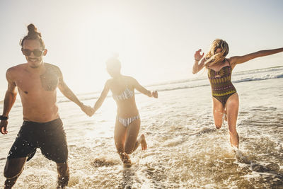 Friends running at beach against clear sky