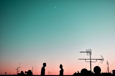 Low angle view of silhouette couple against clear sky at sunset